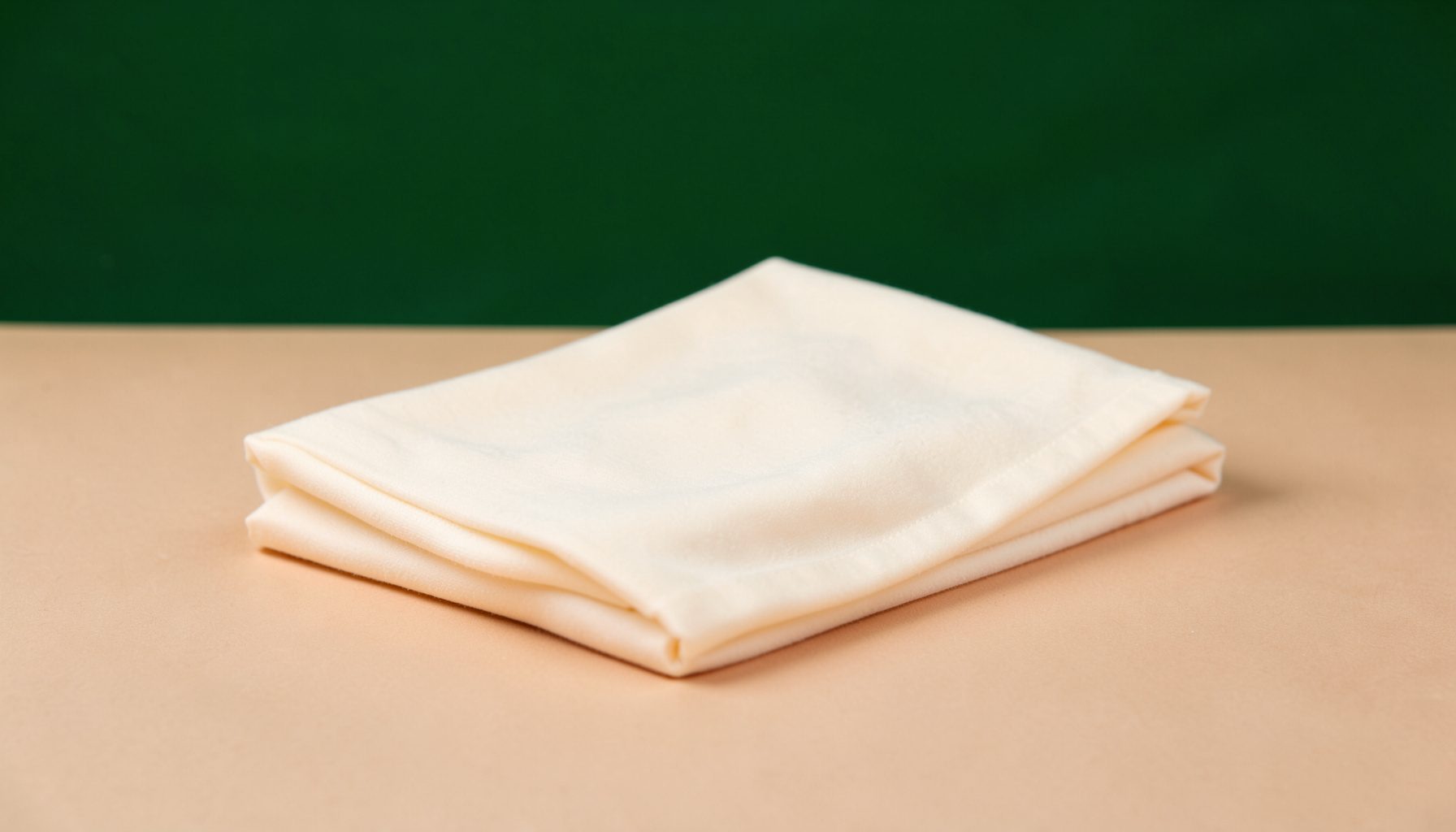 Soft cream-colored folded traditional Japanese fabric resting on a warm beige surface, gentle diffused light